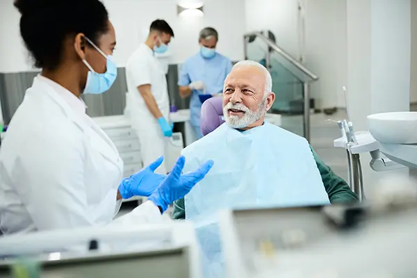 Older white patient sitting in dental chair calmly discussing his oral health with his dentist